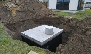 Instalacja odprowadzenia wody z rynien do gruntu. W wykopie widoczny betonowy zbiornik z włazem.