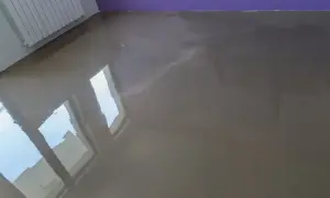 Lśniąca, szara posadzka, przypominająca polerowaną terakotę, odbija światło z okien.