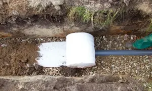 Budowa drenażu: rura drenarska owinięta geowłókniną, otoczona żwirem i ziemią.