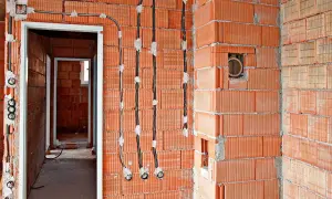 Instalacja elektryczna bezpuszkowa w budowie. Widoczne kable i puszki instalacyjne w ścianach z cegły.