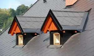 Dwa lukarny z drewnianymi szczytami i okienkami na szarym dachu jednospadowym.