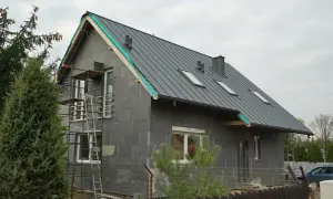 Dom w trakcie budowy, z szarym dachem i oknami dachowymi. Rusztowania przy ścianie. Remont starego domu od czego zacząć? Od fundamentów i ścian!