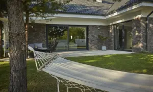 Hamak w ogrodzie nowoczesnego bungalow z ceglaną elewacją i dużymi przeszkleniami.