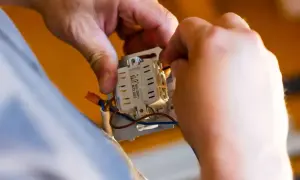 Ręce elektryka podłączają przewody do mechanizmu włącznika. Dowiedz się, ile kosztuje przyłącze prądu.