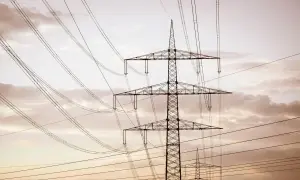 Wysoki słup na działce, który stoi tam od ponad 30 lat, otoczony siecią przewodów elektrycznych na tle zachmurzonego nieba.
