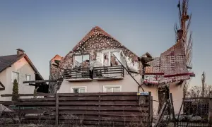 Zniszczony dom po ostrzale. Rozbiórka dachu i ścian, wybite okna, zniszczony płot.