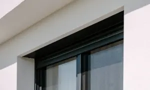 Czarne, przesuwne okno z siatką przeciw owadom, w białej, otynkowanej ścianie. Różne rodzaje okien oferują różne funkcje.