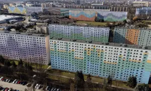 Kolorowe bloki z wielkiej płyty tworzą mozaikę na tle miasta. Długie, wielopiętrowe budynki pokryte są pastelowymi barwami: fioletem, zielenią, błękitem i pomarańczem.