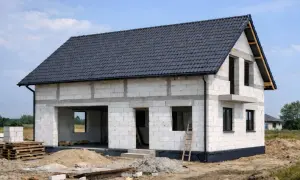 Dom w budowie, widoczne etapy budowy domu: ściany z bloczków, dach pokryty dachówką, otwory okienne i drzwiowe.