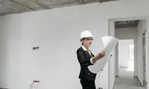Kobieta w kasku i okularach analizuje plany budowy w niedokończonym wnętrzu.
