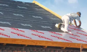 Pracownik montuje ocieplenie nakrokwiowe na dachu, układając warstwy izolacji i membrany.