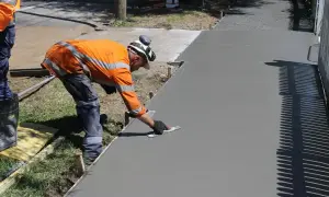 Robotnik wygładza świeży beton B25. Cena za m3 jest kluczowa przy planowaniu budowy chodnika.