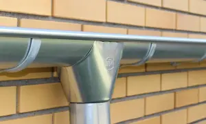 Rynna i rura spustowa z metalu, zabezpieczone galwanizacją, zamontowane na żółtej ceglanej ścianie.