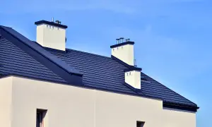 Nowy dom z ciemnym dachem i białymi kominami. Przepustnica wentylacyjna na jednym z kominów.