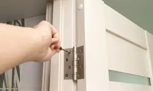 Dłoń dokręca śrubę w zawiasie drzwi, wykonując regulację zawiasów drzwi.