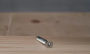 Metalowy konfirmat leży na drewnianym blacie.