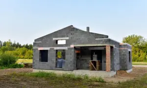 Budowa domu z keramzytu. Widoczne otwory okienne i drzwiowe, szary beton, zielone drzewa w tle.