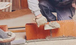 Murarz w rękawicach nakłada zaprawę na pustak, budując ścianę.