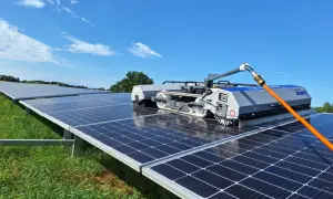 Robot do mycia paneli fotowoltaicznych czyści rzędy paneli na zielonej łące pod błękitnym niebem.