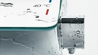 Chromowany termostat prysznicowy z kropelkami wody. Wskaźnik pokazuje 40°C, a niebieski i czerwony pasek sugerują, z której strony ciepła woda.