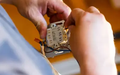 Ręce elektryka podłączają przewody do mechanizmu włącznika. Dowiedz się, ile kosztuje przyłącze prądu.