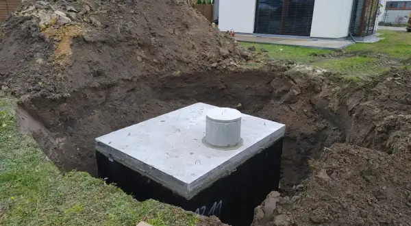 Instalacja odprowadzenia wody z rynien do gruntu. W wykopie widoczny betonowy zbiornik z włazem.