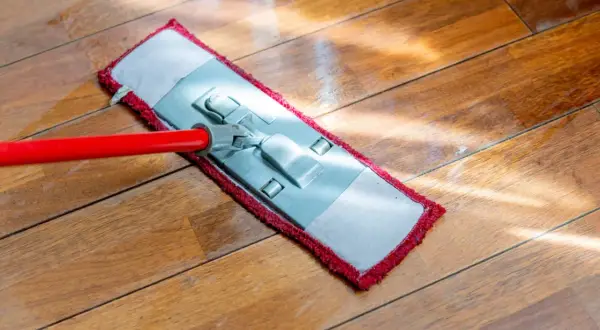 Mop z czerwoną rączką myje drewnianą podłogę.