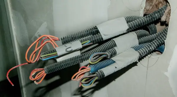 W ścianie widać wiązki przewodów w peszlach. Czy czerwony to plus, czy minus? Instalacja elektryczna w trakcie budowy.