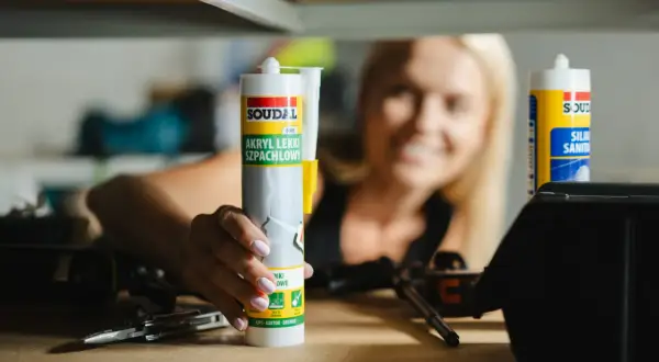 Kobieta trzyma tubkę akrylu lekkiego szpachlowego Soudal. Akryl to wszechstronny materiał budowlany.
