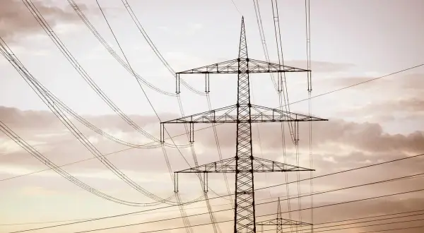 Wysoki słup na działce, który stoi tam od ponad 30 lat, otoczony siecią przewodów elektrycznych na tle zachmurzonego nieba.