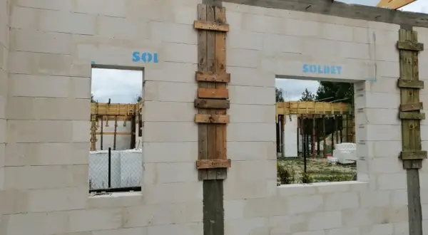 Ściana z bloczków z otworami okiennymi i drewnianymi szalunkami, w trakcie budowy.