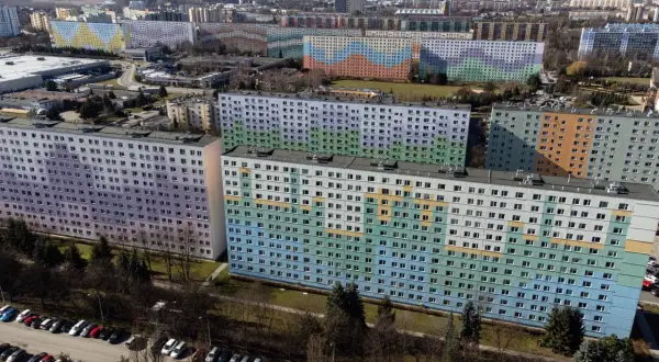 Kolorowe bloki z wielkiej płyty tworzą mozaikę na tle miasta. Długie, wielopiętrowe budynki pokryte są pastelowymi barwami: fioletem, zielenią, błękitem i pomarańczem.