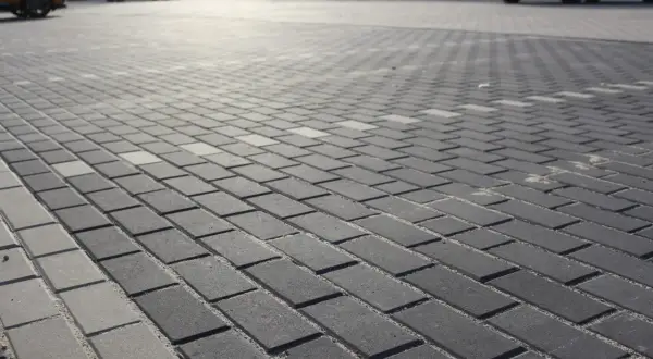 Szary parking wyłożony kostką holland. W tle widać zaparkowane samochody.