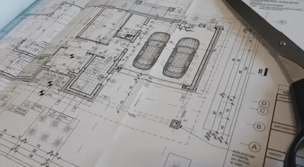 Projekt architektoniczno budowlany domu z garażem, nożyczki przecinają plany.