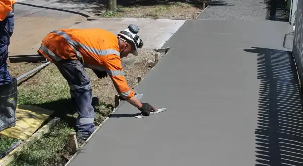 Robotnik wygładza świeży beton B25. Cena za m3 jest kluczowa przy planowaniu budowy chodnika.
