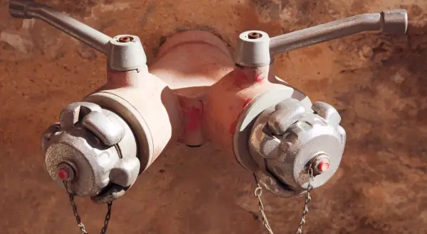Czerwony hydrant podziemny z dwoma metalowymi zaworami i łańcuszkami, gotowy do akcji.