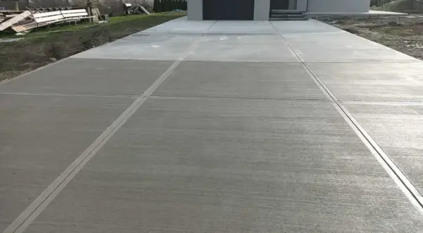 Nowy podjazd z beton stemplowany, z wyraźnymi liniami podziału, prowadzi do nowoczesnego domu.
