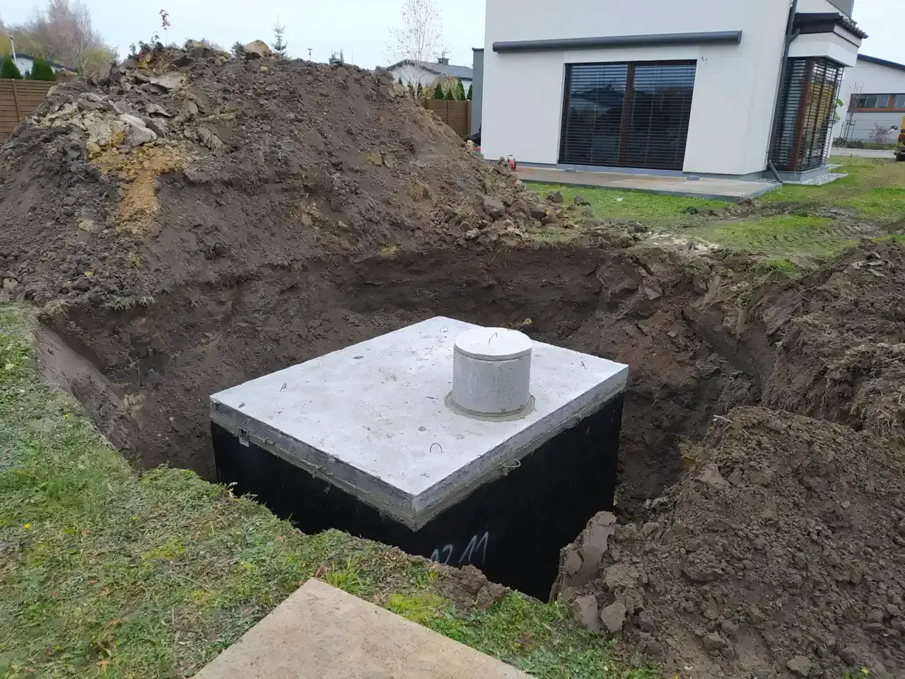 Instalacja odprowadzenia wody z rynien do gruntu. W wykopie widoczny betonowy zbiornik z włazem.