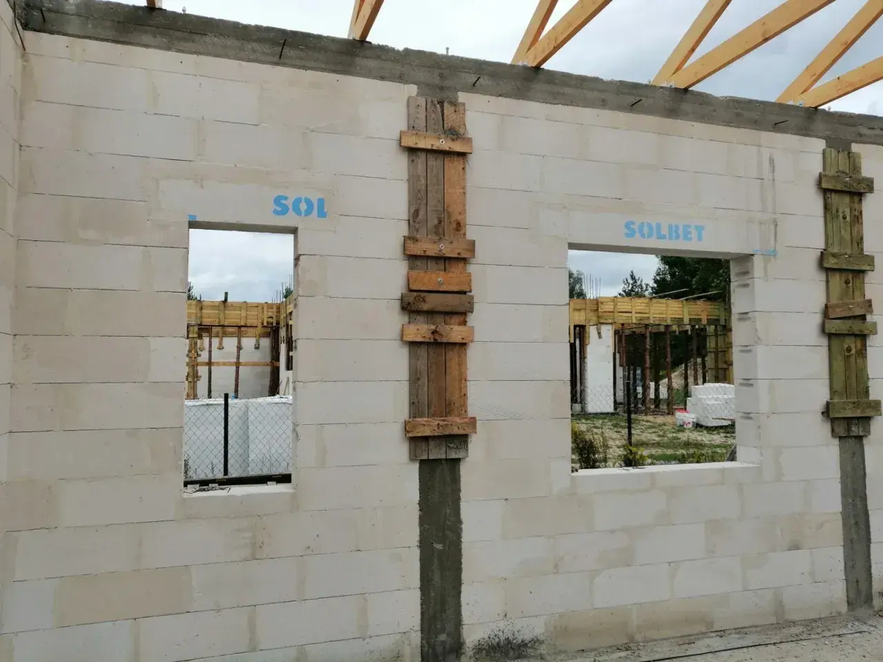 Ściana z bloczków z otworami okiennymi i drewnianymi szalunkami, w trakcie budowy.