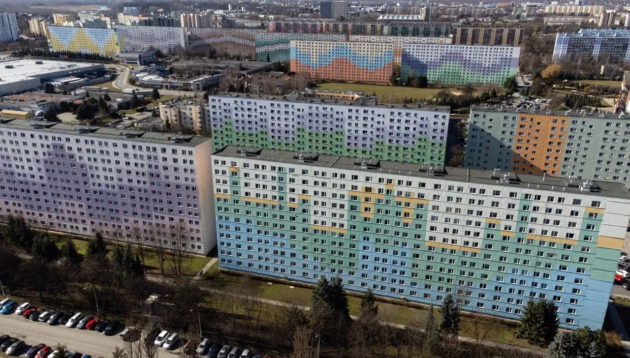 Kolorowe bloki z wielkiej płyty tworzą mozaikę na tle miasta. Długie, wielopiętrowe budynki pokryte są pastelowymi barwami: fioletem, zielenią, błękitem i pomarańczem.