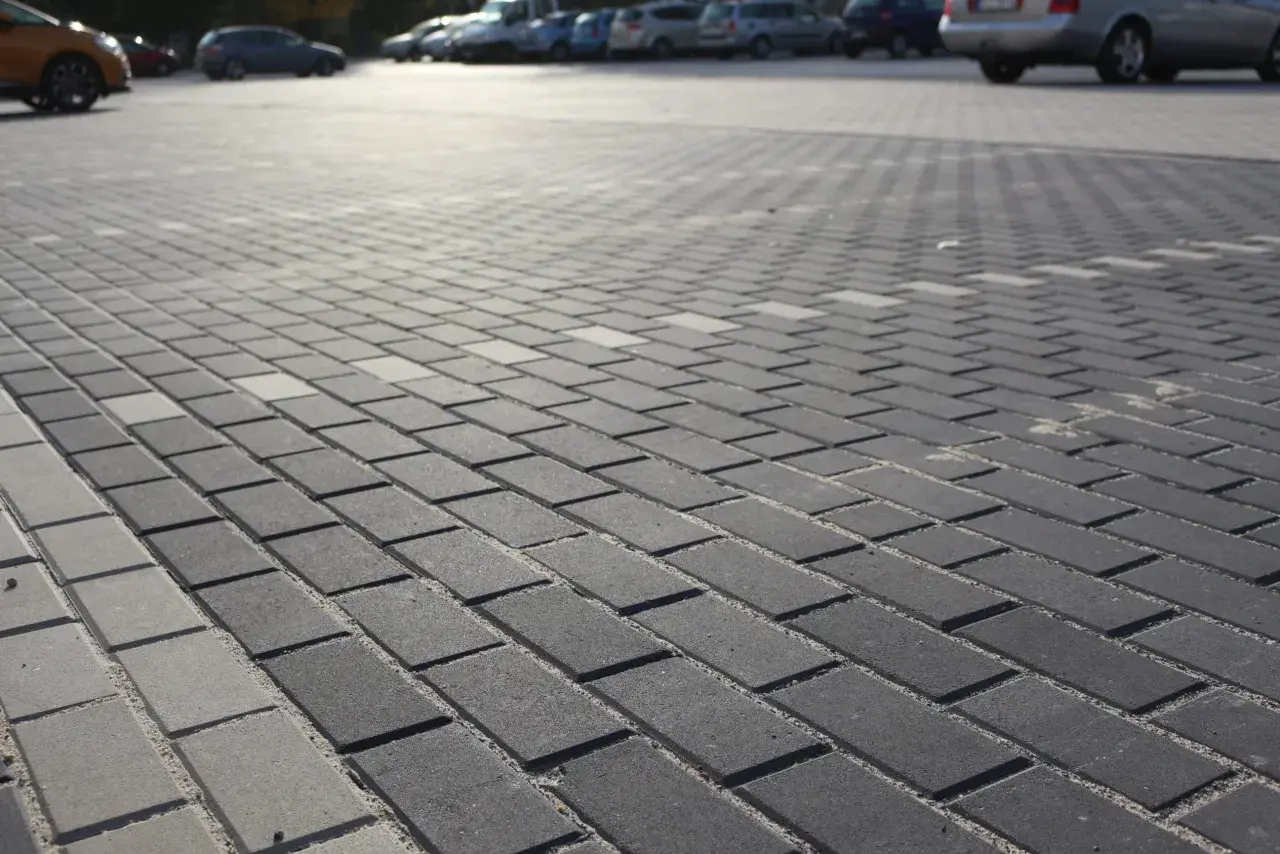 Szary parking wyłożony kostką holland. W tle widać zaparkowane samochody.