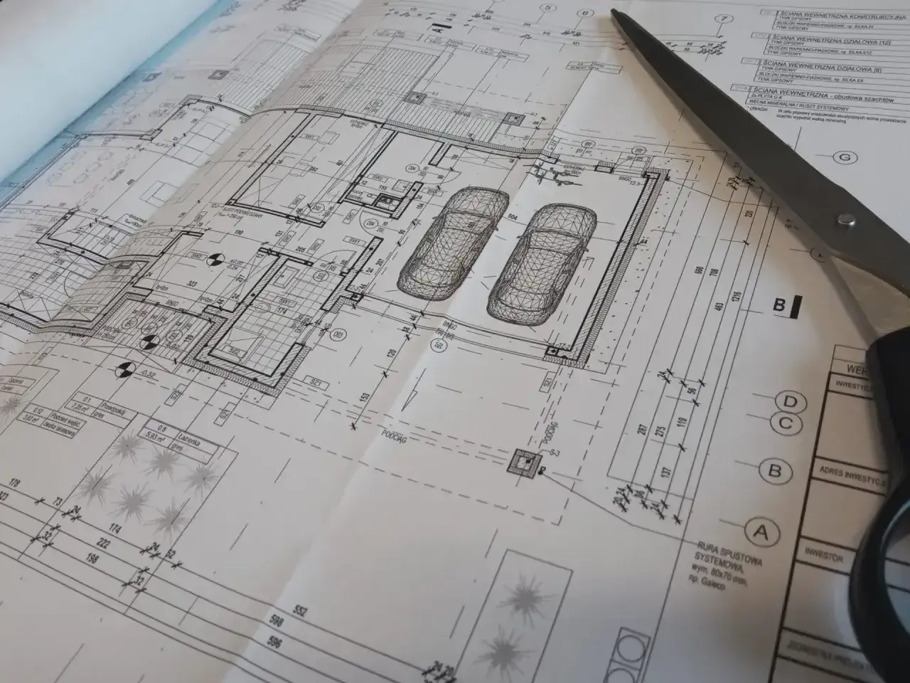 Projekt architektoniczno budowlany domu z garażem, nożyczki przecinają plany.