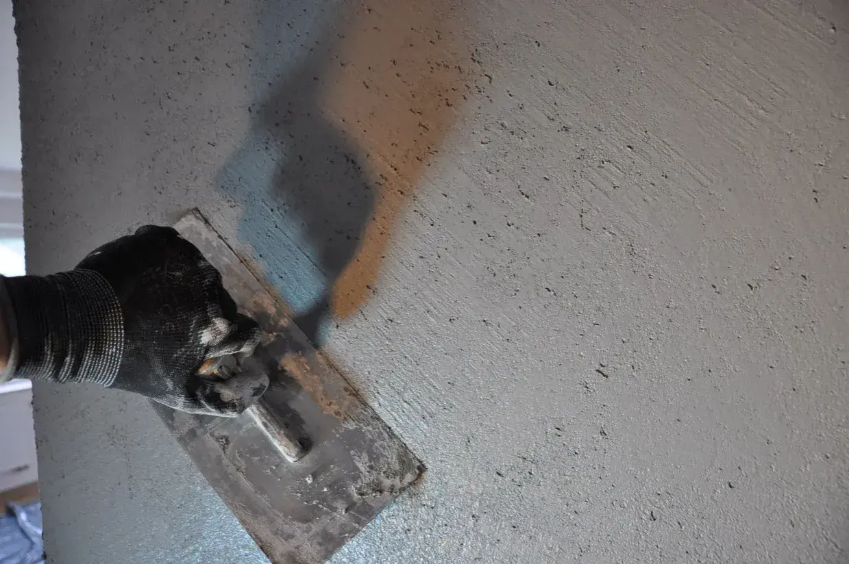 Ręka w rękawicy wygładza świeżą zaprawę, pokazując, jak zrobić beton. Cień narzędzia rzuca się na chropowatą powierzchnię.