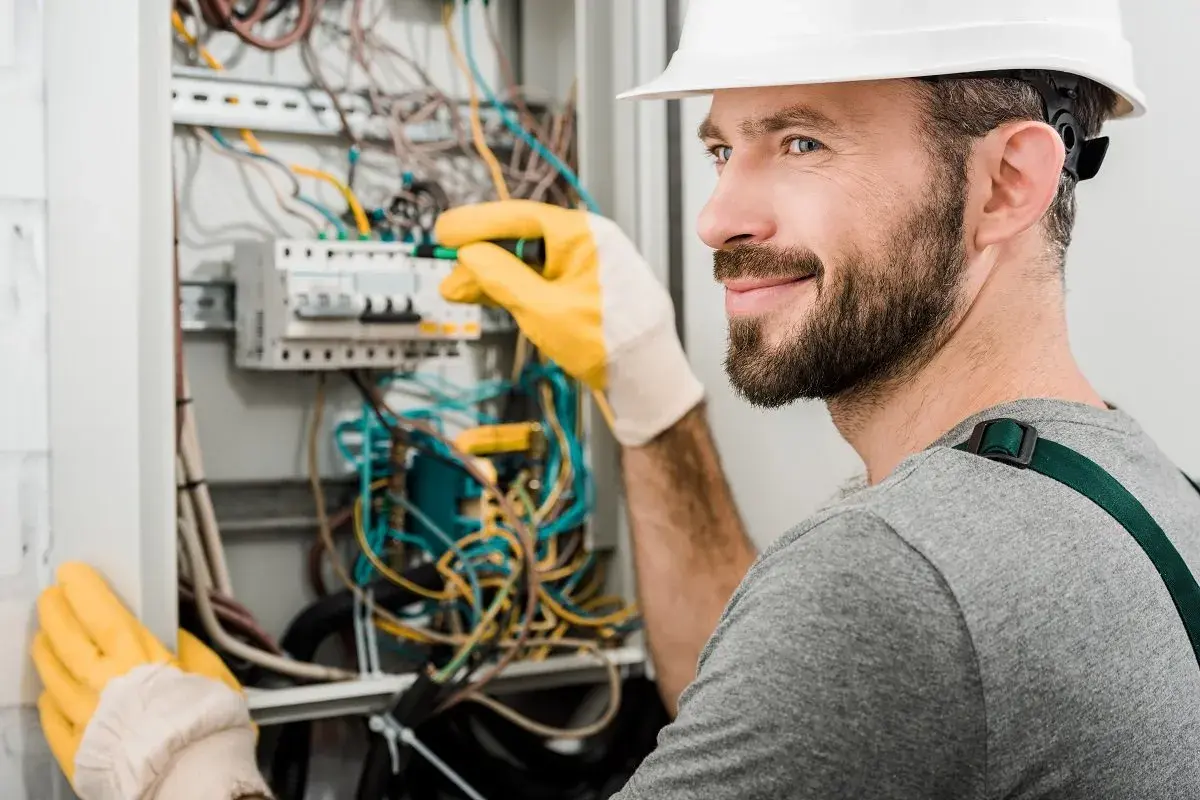 Elektryk z uprawnieniami SEP do 1kV pracuje przy rozdzielnicy, poprawiając okablowanie.