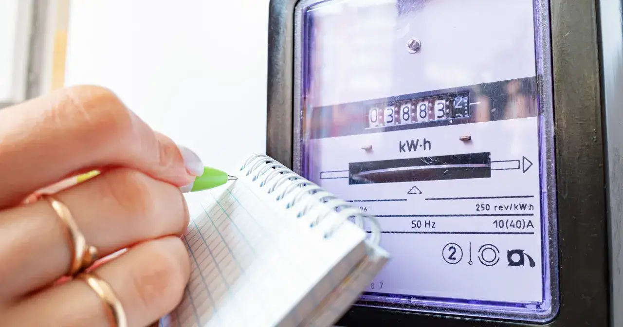 Dłoń z zielonym długopisem zapisuje odczyt licznika energii elektrycznej, kontrolując dodatek do prądu.