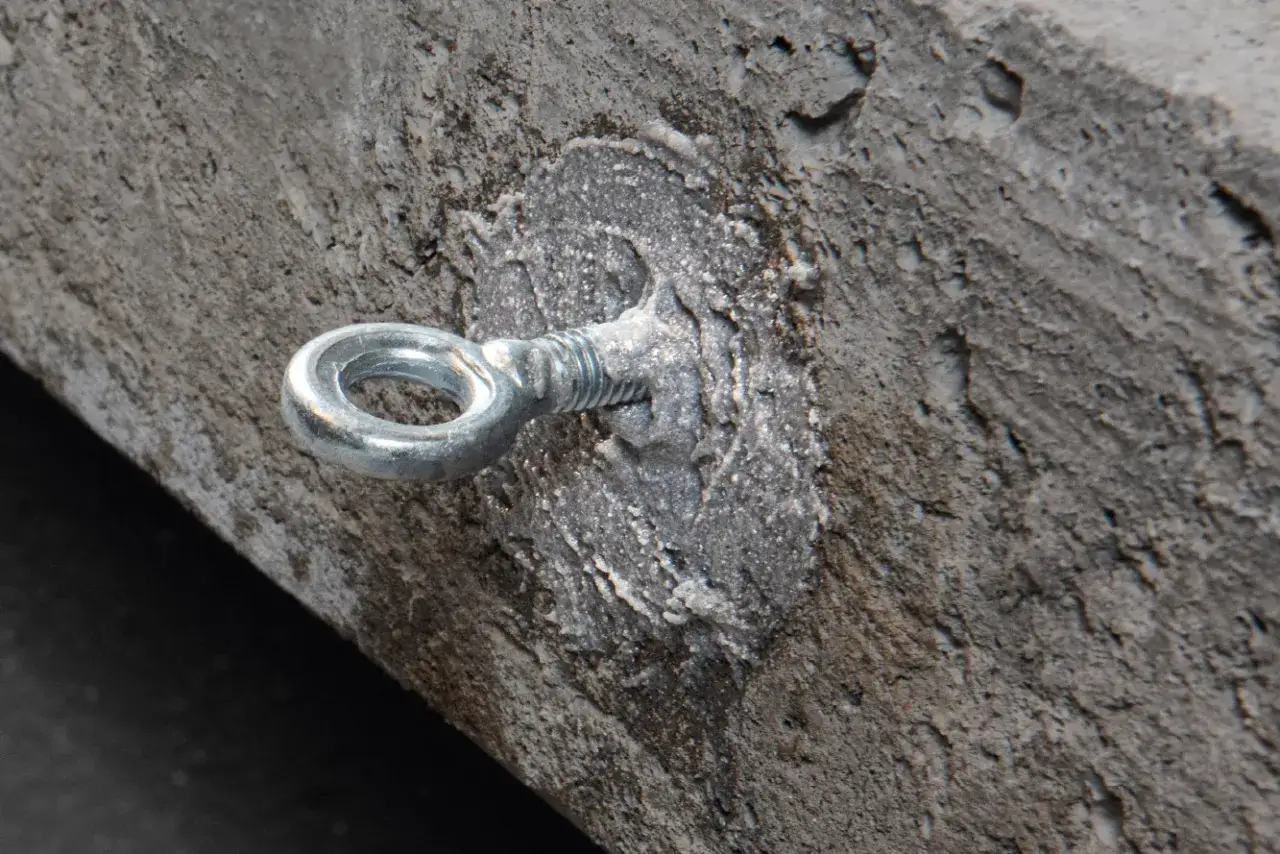 Metalowe oczko wkręcone w beton, zabezpieczone masą, która przypomina kotwy chemiczne.