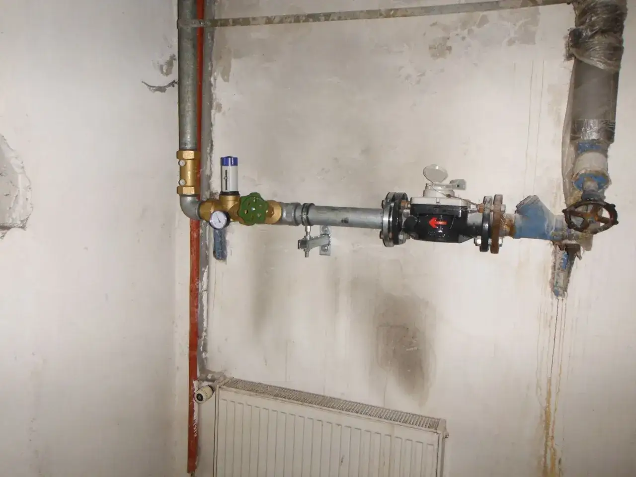 Instalacja wodna z widocznym licznikiem i zaworem, a także elementem przypominającym reduktor ciśnienia.