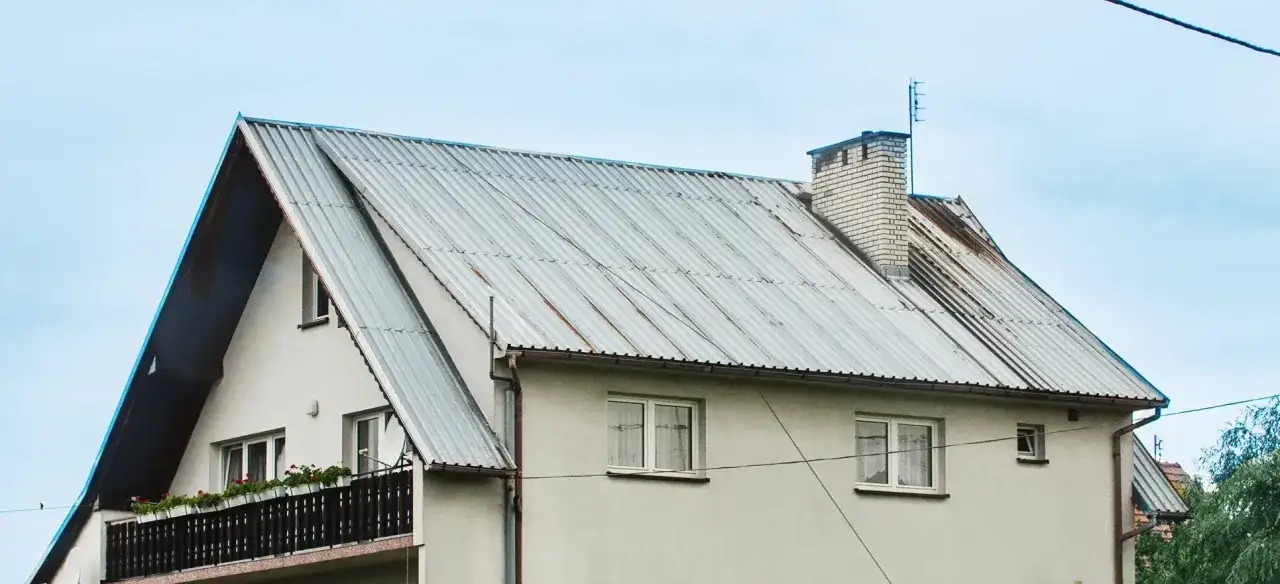 Szary, falisty dach domu z kominem. Zastanawiasz się nad malowanie dachu cena?