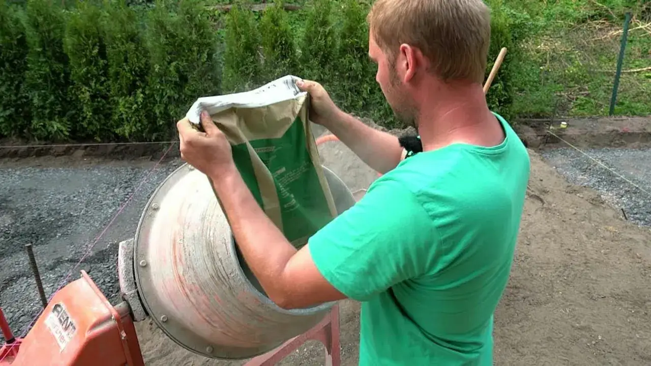Mężczyzna w zielonej koszulce wsypuje cement do betoniarki, pokazując, jak zrobić beton.