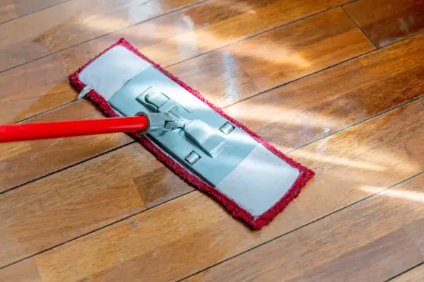 Mop z czerwoną rączką myje drewnianą podłogę.